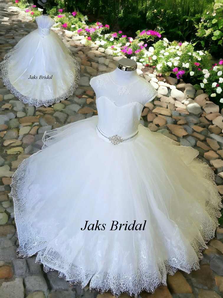 Lace illusion flower girl wedding dress with a sweetheart neckline and sleeves. Completed with a beaded sash, and elegant lace train.