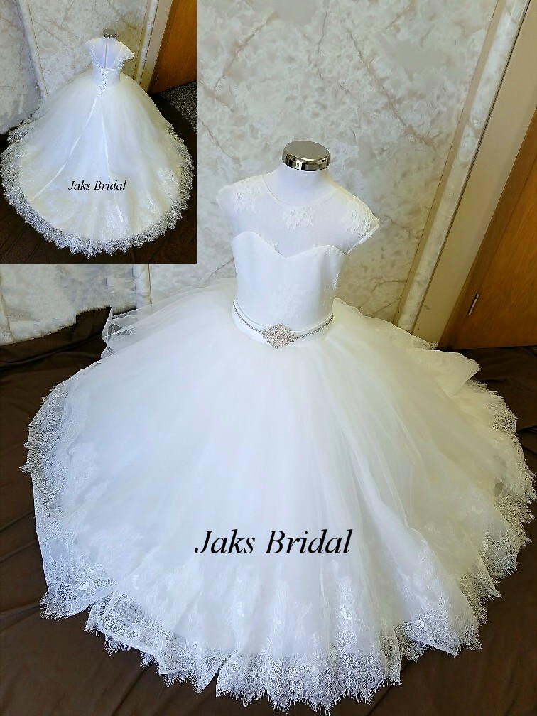 Lace illusion flower girl wedding dress with a sweetheart neckline and sleeves. Completed with a beaded sash, and elegant lace train.